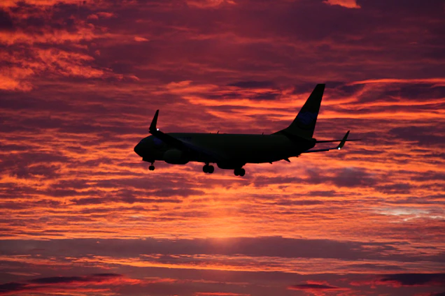A breathtaking high-resolution photo capturing a vibrant sunset sky with a silhouette of a soaring airplane.