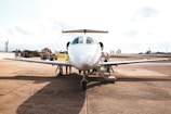 A private jet is parked on an airport tarmac with a refueling truck nearby. Several people, likely ground crew, are seen around the aircraft, working on or inspecting it. The background includes a clear sky and some distant city buildings.