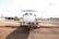 A private jet is parked on an airport tarmac with a refueling truck nearby. Several people, likely ground crew, are seen around the aircraft, working on or inspecting it. The background includes a clear sky and some distant city buildings.