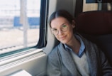 Model seated by a window, wearing a cozy layered outfit with muted earth tones.