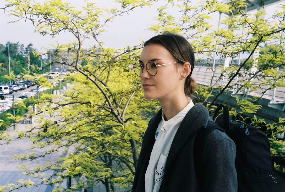 a woman wearing glasses standing in front of a tree