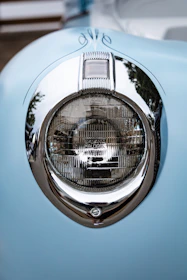 Close-up of a vintage car's headlight reflecting the surrounding forest in soft morning light.