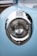 A close-up view of a vintage car's headlight featuring intricate chrome detailing and a soft blue paint finish. The design includes classic pinstriping around the light, and the reflection of trees and sky can be seen on the chrome surface.