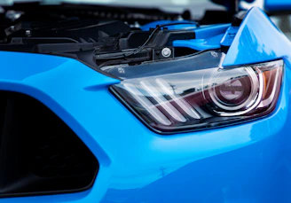 Close-up of a sleek sports car headlight glowing with bright blue LED accents in a dark garage.
