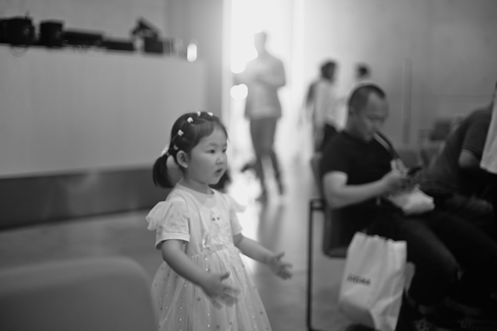 a little girl in a white dress standing in a room
