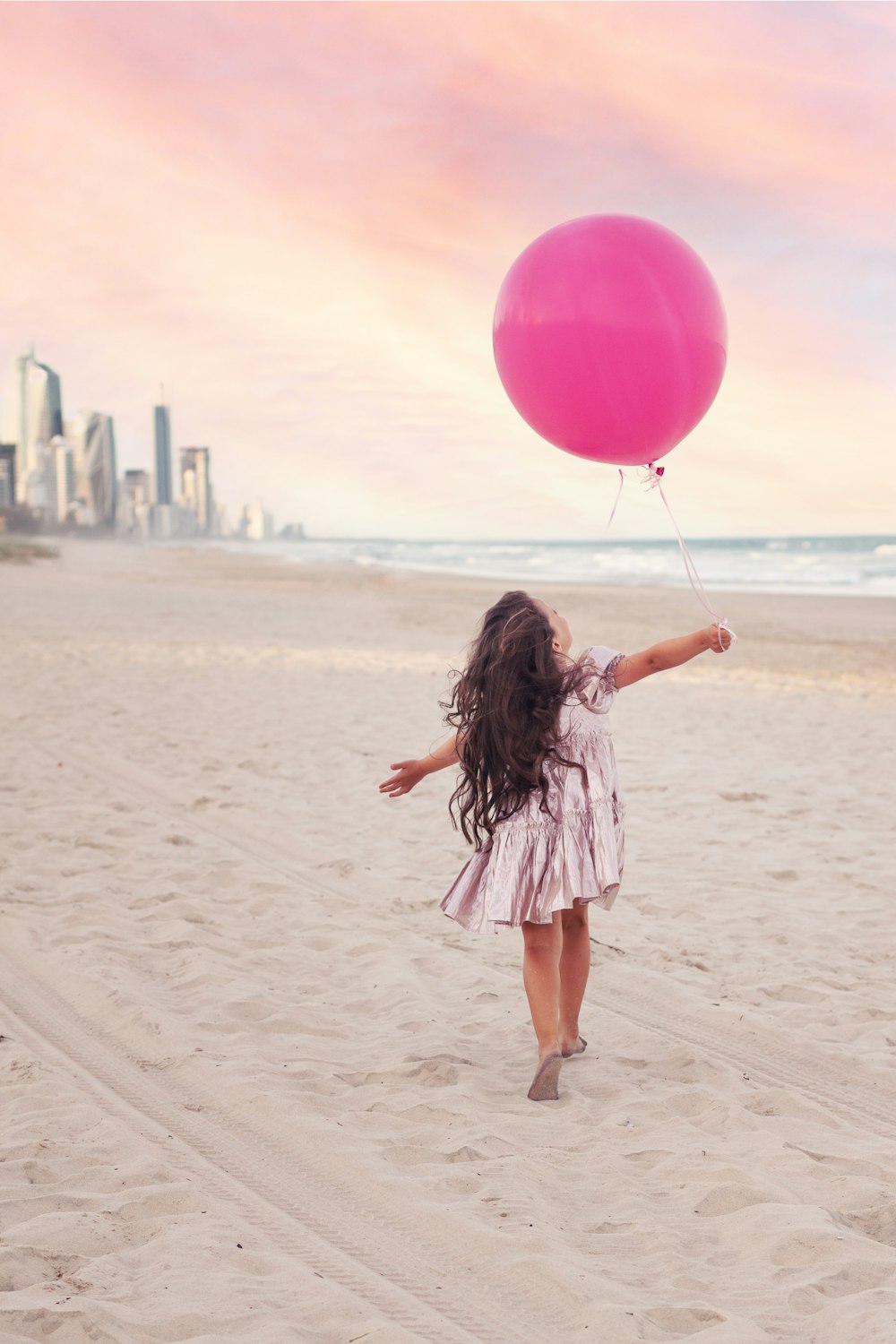 a little girl running on the beach with a pink balloon