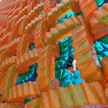 A complex and abstract 3D structure composed of interlocking geometric shapes with a glossy, textured surface. The colors are vibrant with a reflective quality, giving a sense of depth and intricate design.