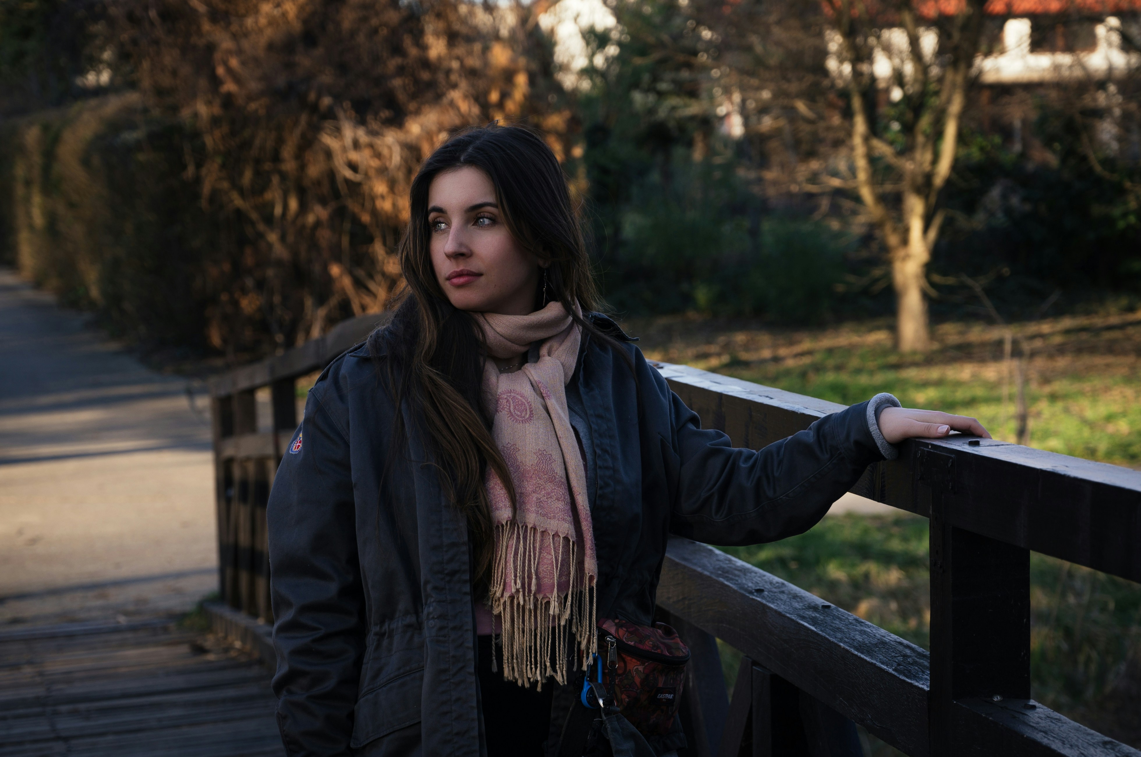 Woman in a coat and scarf on a timber bridge in a park