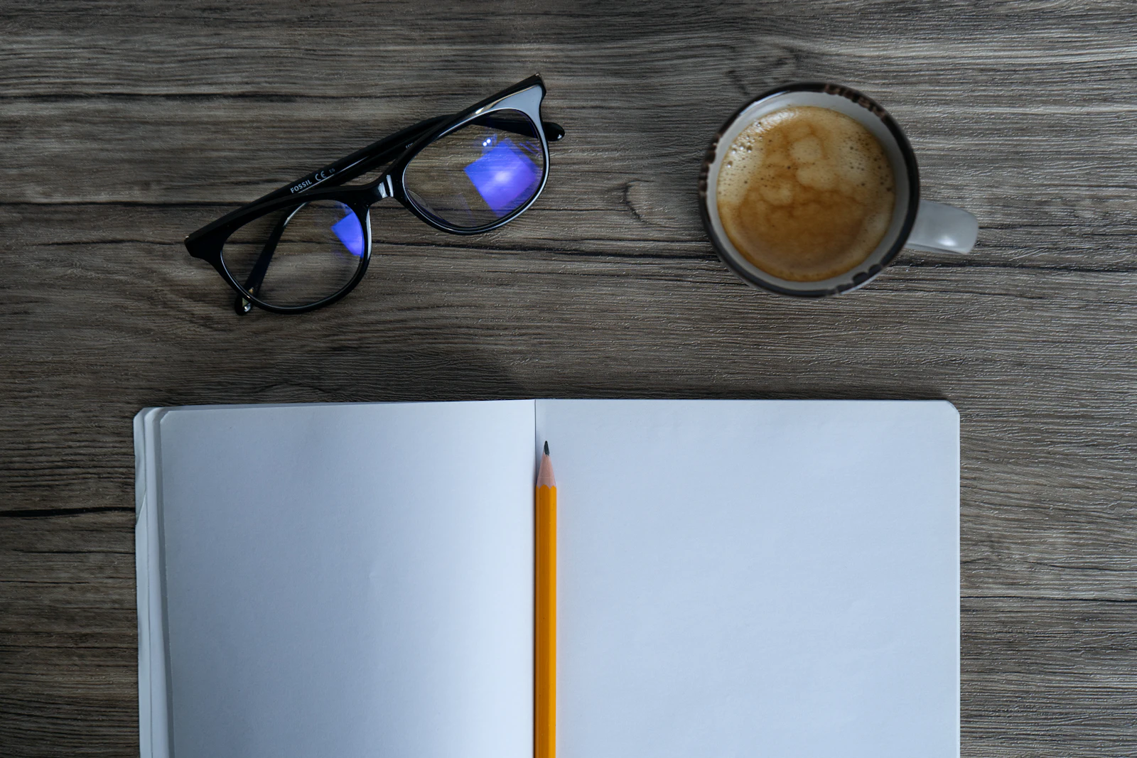 An open notebook with a pencil and a cup of coffee on a desk