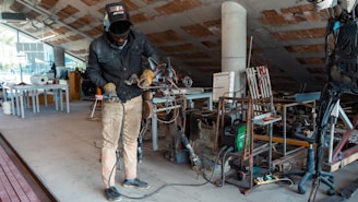 A friendly welder answering a phone call in a workshop with tools and metalwork around.
