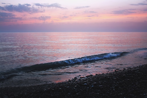A peaceful coastline at sunset with waves gently lapping against rocky shores.