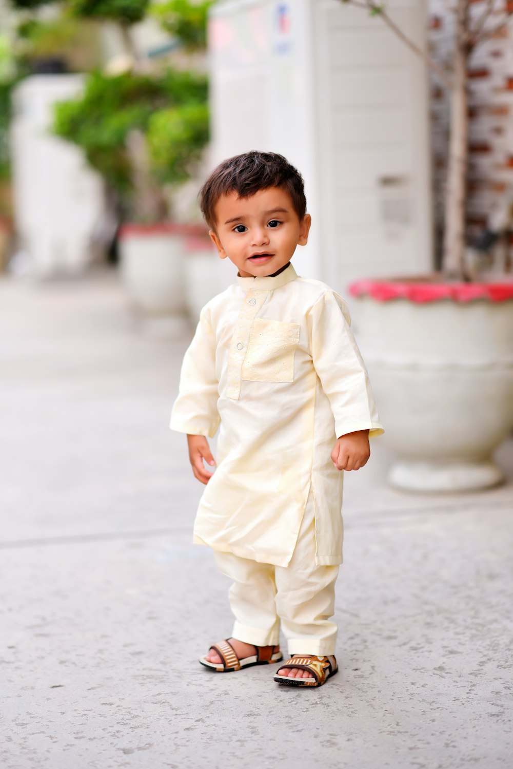 a little boy in a white outfit standing on a sidewalk