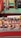 A collection of handcrafted ceramic cups, bowls, and pottery pieces displayed on a table with a patterned cloth. Colorful scarves hang in the background, adding vibrancy to the scene. The pottery includes various intricate designs, with a focus on earthy tones and patterns.
