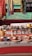 A collection of handcrafted ceramic cups, bowls, and pottery pieces displayed on a table with a patterned cloth. Colorful scarves hang in the background, adding vibrancy to the scene. The pottery includes various intricate designs, with a focus on earthy tones and patterns.