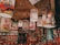 A ceiling display features hanging lampshades adorned with colorful and whimsical cartoon illustrations. The shelves below are stocked with a variety of mugs and other merchandise featuring similar cartoon art. The overall setting seems to be a gift shop or a similar retail space filled with vibrant and humorous cartoon-themed products.