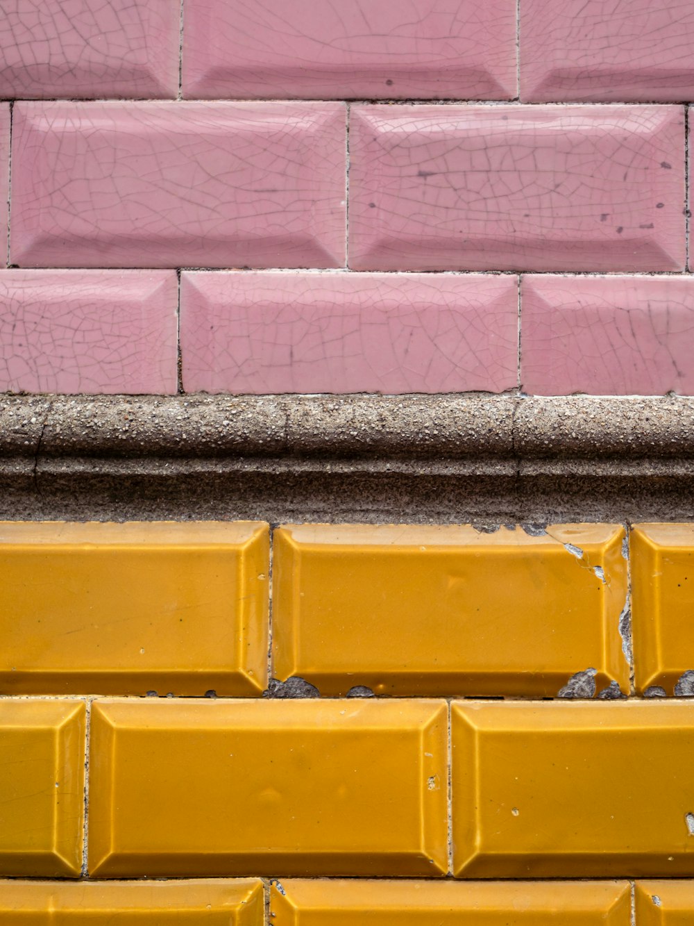 a yellow bench sitting next to a pink brick wall