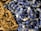 A close-up of various polished stones strung together in necklaces, featuring an assortment of blue and brown tones. The stones have a glossy finish, highlighting their smooth, rounded shapes.