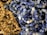 A close-up of various polished stones strung together in necklaces, featuring an assortment of blue and brown tones. The stones have a glossy finish, highlighting their smooth, rounded shapes.