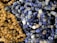 A close-up of various polished stones strung together in necklaces, featuring an assortment of blue and brown tones. The stones have a glossy finish, highlighting their smooth, rounded shapes.
