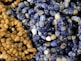 A close-up of various polished stones strung together in necklaces, featuring an assortment of blue and brown tones. The stones have a glossy finish, highlighting their smooth, rounded shapes.