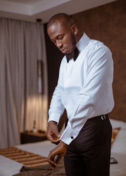 A groom adjusting his cufflinks in a softly lit room, capturing quiet anticipation.