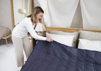 a woman putting a blue blanket on top of a bed