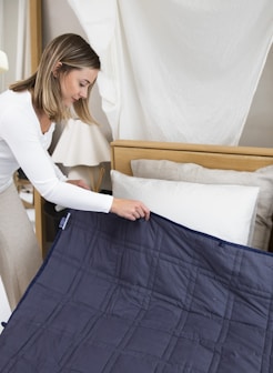 a woman putting a blue blanket on top of a bed