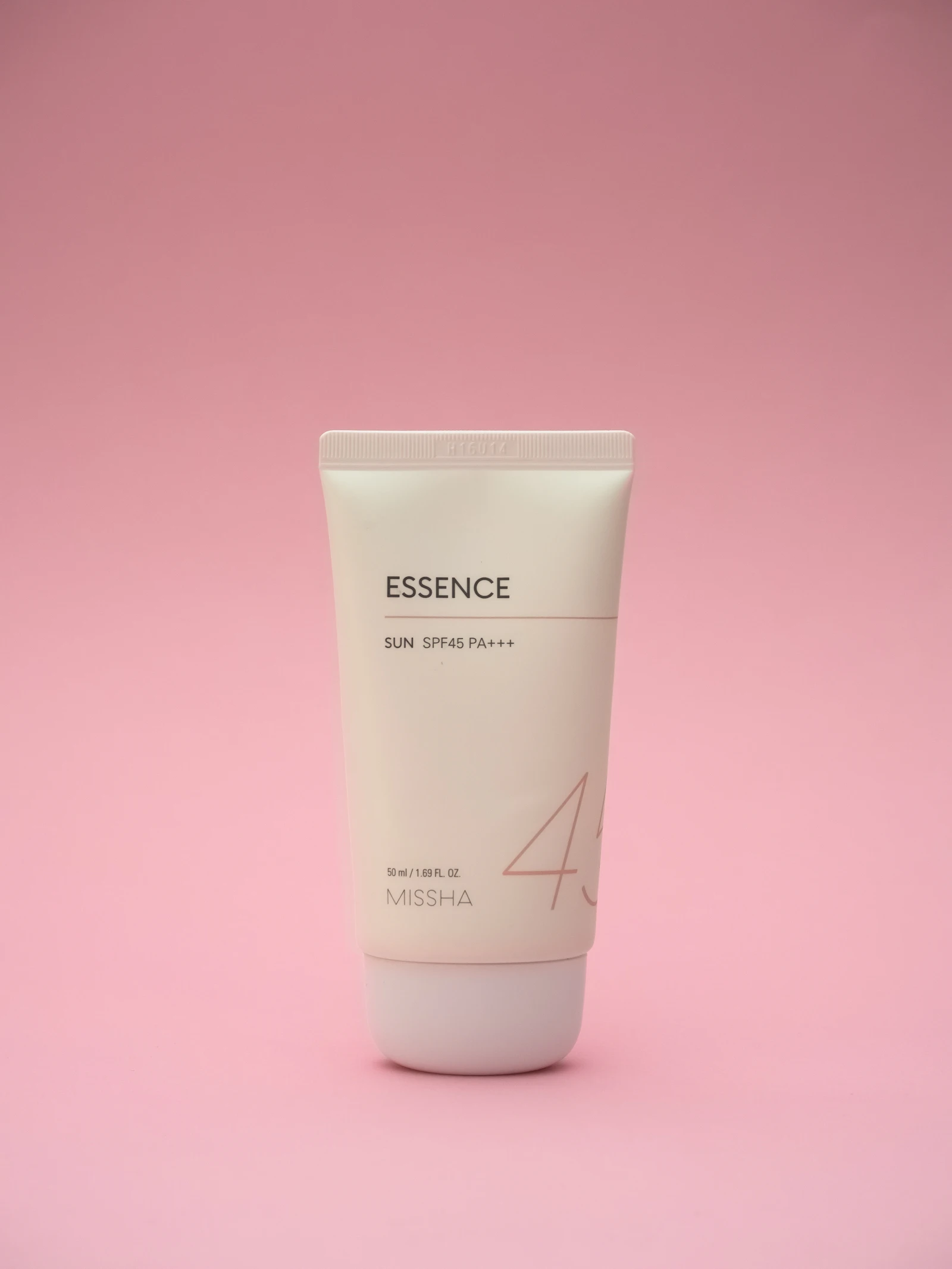 A tube of skincare cream against a soft pink background, representing a Korean sunscreen comparison