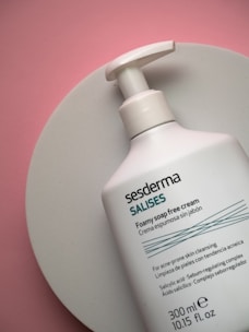 A bottle of foamy soap-free cream from the brand Sesderma is placed on a round white surface. The bottle is predominantly white with teal and black text, and includes product details and ingredients.