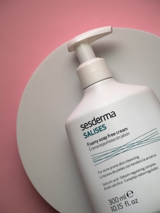 A bottle of foamy soap-free cream from the brand Sesderma is placed on a round white surface. The bottle is predominantly white with teal and black text, and includes product details and ingredients.