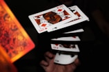 A series of playing cards appear to be floating in mid-air, capturing a dynamic moment possibly from a magic trick or cardistry performance. The cards are fanned out, aligning symmetrically as a hand beneath adds a sense of motion. The focus is sharp on the cards, highlighting their detailed patterns and suits.