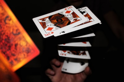 A series of playing cards appear to be floating in mid-air, capturing a dynamic moment possibly from a magic trick or cardistry performance. The cards are fanned out, aligning symmetrically as a hand beneath adds a sense of motion. The focus is sharp on the cards, highlighting their detailed patterns and suits.