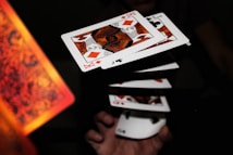 A series of playing cards appear to be floating in mid-air, capturing a dynamic moment possibly from a magic trick or cardistry performance. The cards are fanned out, aligning symmetrically as a hand beneath adds a sense of motion. The focus is sharp on the cards, highlighting their detailed patterns and suits.
