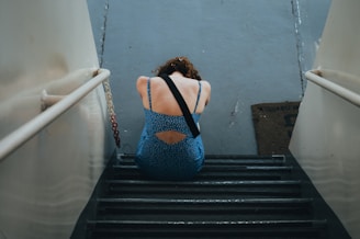 a woman in a blue dress is sitting on a set of stairs