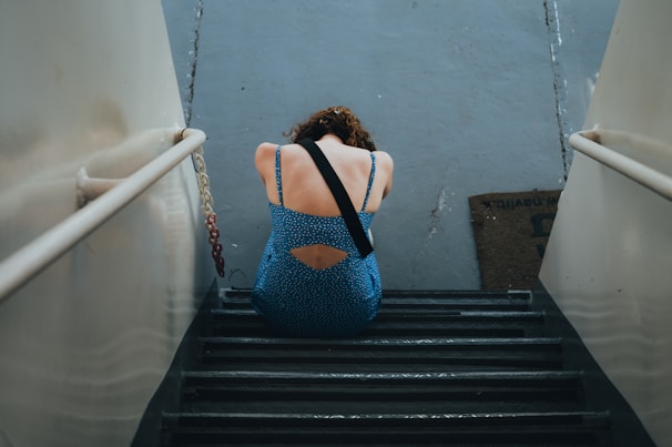 a woman in a blue dress is sitting on a set of stairs