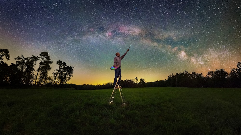 a man is standing on a tripod and pointing at the stars