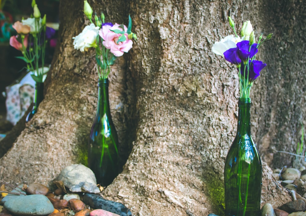 three green glass bottles with flowers in them