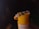 A bracelet with colorful beads, including blue, black, and white, is draped over the top of a yellow cylindrical container. The bracelet features a central metallic circular element with spiral grooves. The background is dark, creating a contrast with the bright foreground.
