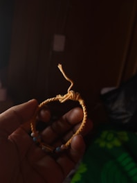 A hand is holding a handmade bracelet with a woven design, made primarily of yellow cord. It includes small beads in varying colors such as blue and black. The background is dark, emphasizing the bracelet.