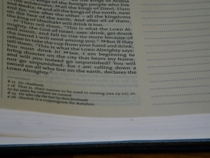 A close-up view of an open book showing text on both left and right pages. The left page contains printed text in a paragraph format with some footnotes at the bottom. The right page is mostly empty with lined spaces for writing notes.