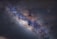 A vibrant image of a galaxy with a dense cluster of stars and stellar dust. The central band appears bright with varying hues of blue, white, and brown, surrounded by darker regions. Tiny specks of light dot the area, creating a celestial and cosmic landscape.