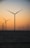 Several wind turbines are situated offshore, their large blades silhouetted against a gradient sky transitioning from orange to blue as the sun sets. The sea is calm and dark in the foreground, adding contrast to the serene landscape.