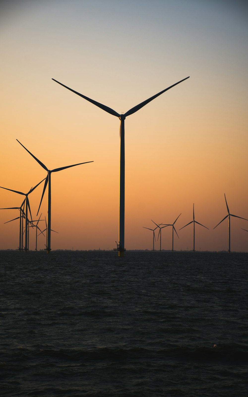 a group of windmills in the ocean at sunset
