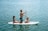 Family laughing together while trying paddleboarding on calm turquoise waters.