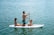 Family laughing together while trying paddleboarding on calm turquoise waters.