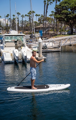 A paddleboard gliding alongside a yacht on a calm sunny afternoon near the marina.