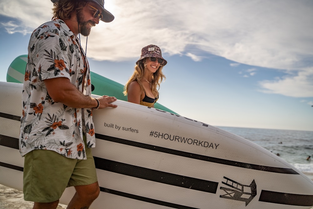 Un homme tenant une planche de surf à côté d'une femme sur la plage photo –  Photo Shorts Gratuite sur Unsplash