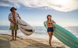 Two friends laughing on the beach, surfboards resting in the sand behind them.