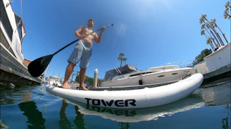 A person balancing on a paddleboard gliding across clear blue water with palm trees in the background.