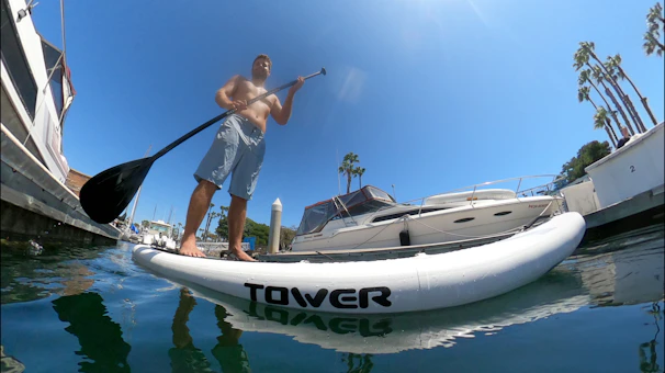 A person balancing on a paddleboard gliding across clear blue water with palm trees in the background.